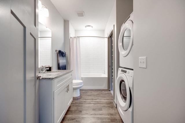 clothes washing area with wood-type flooring, stacked washer and dryer, and sink