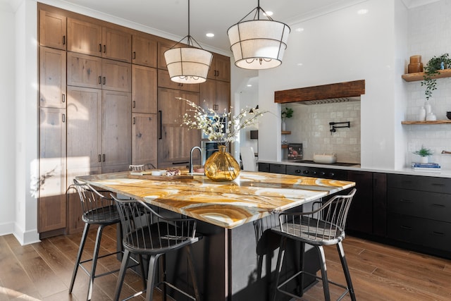 kitchen featuring a breakfast bar area, hardwood / wood-style floors, a kitchen island with sink, decorative backsplash, and light stone counters