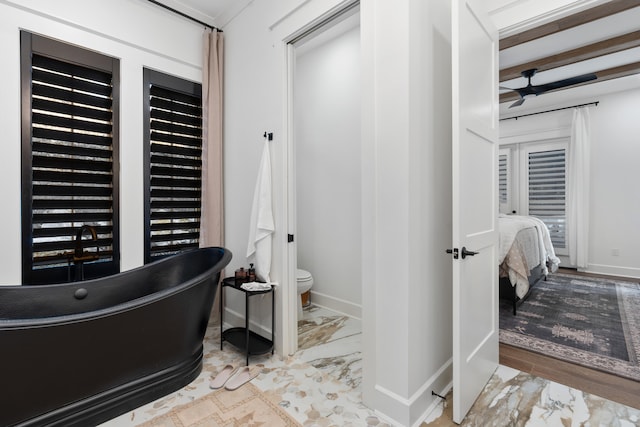 interior space featuring beamed ceiling, toilet, and a bathtub