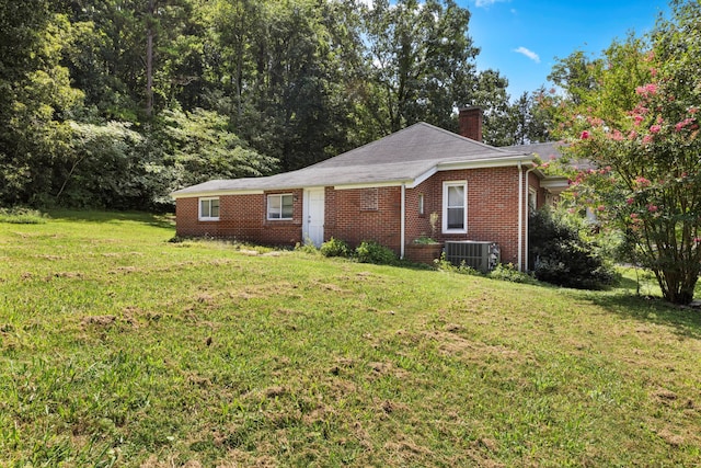 view of side of property featuring a chimney, brick siding, central AC, and a lawn