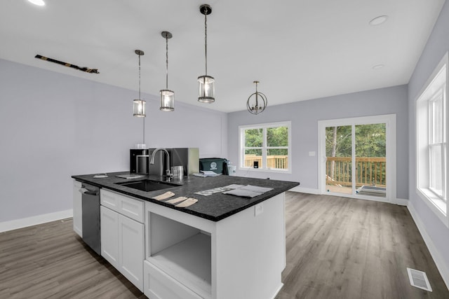 kitchen with decorative light fixtures, dishwasher, an island with sink, sink, and hardwood / wood-style flooring