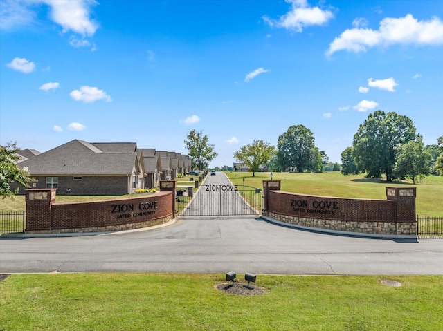 community sign with a gate, fence, and a yard