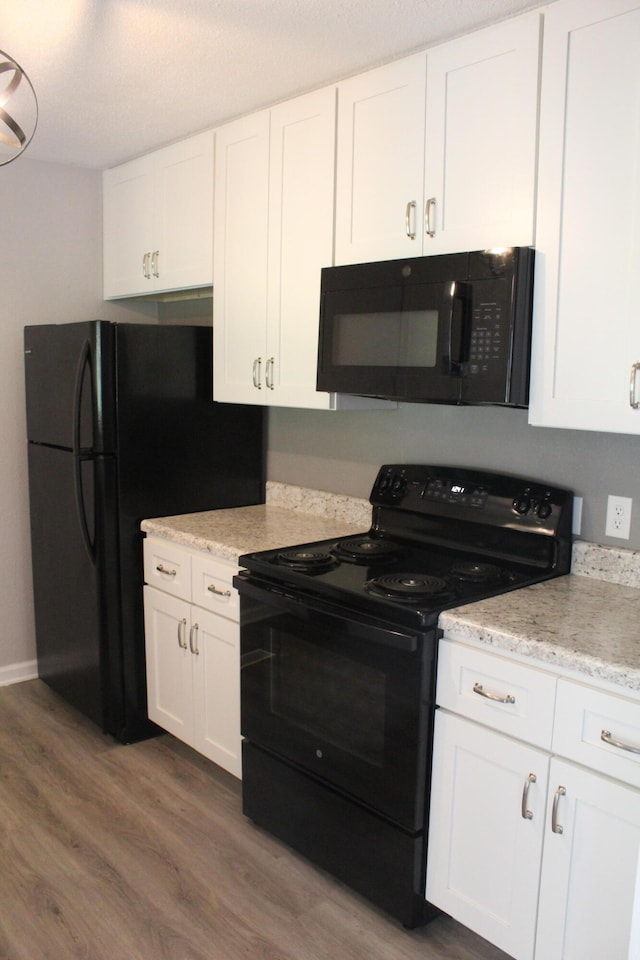 kitchen with light wood-type flooring, black appliances, light stone countertops, and white cabinets