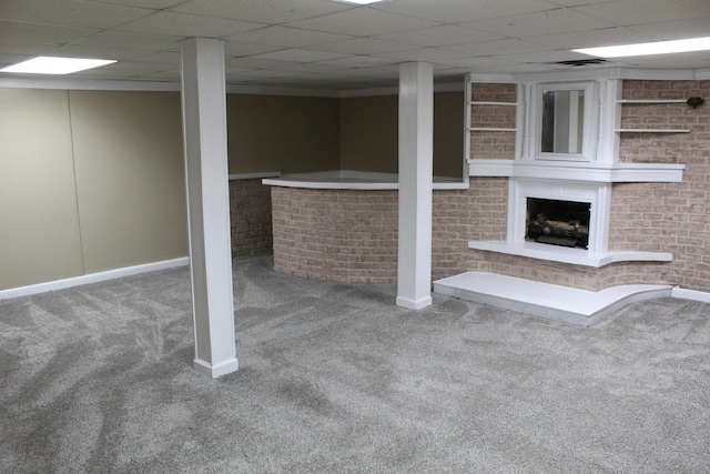 basement featuring carpet flooring, a drop ceiling, and brick wall