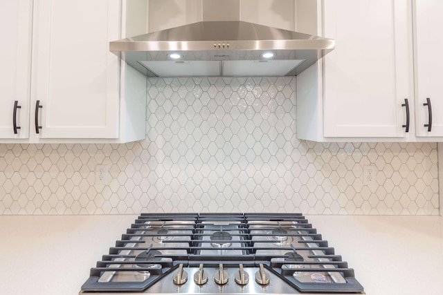 kitchen featuring gas stovetop, backsplash, white cabinetry, and wall chimney range hood