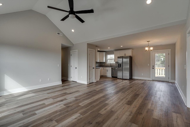 unfurnished living room with ceiling fan with notable chandelier, high vaulted ceiling, and hardwood / wood-style floors