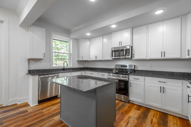 kitchen with appliances with stainless steel finishes, white cabinets, a center island, and dark wood-type flooring