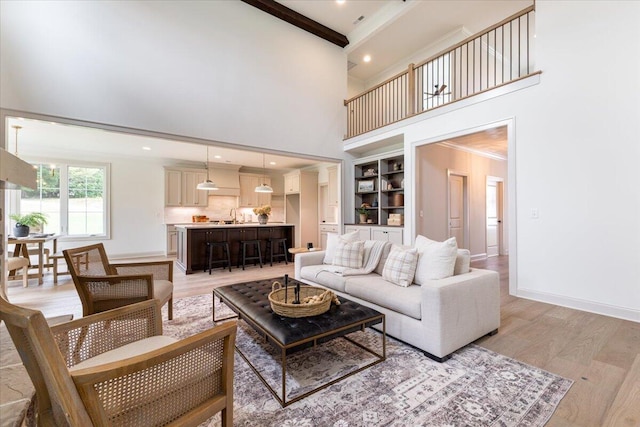 living room featuring beamed ceiling, light hardwood / wood-style floors, ornamental molding, sink, and a towering ceiling