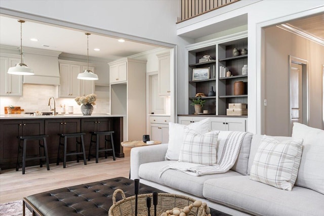 living room featuring ornamental molding, sink, and light hardwood / wood-style floors