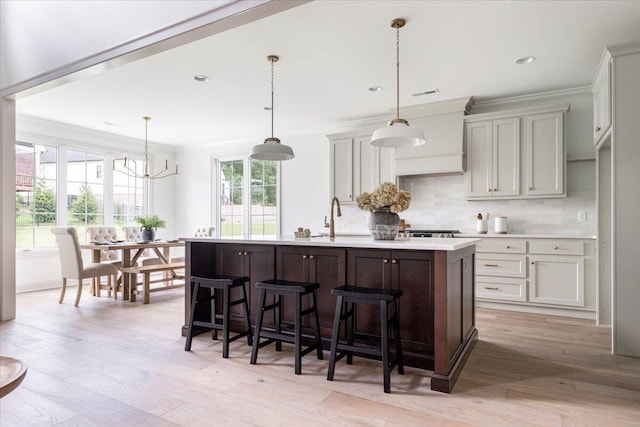 kitchen with hanging light fixtures, backsplash, a kitchen island with sink, and light hardwood / wood-style flooring