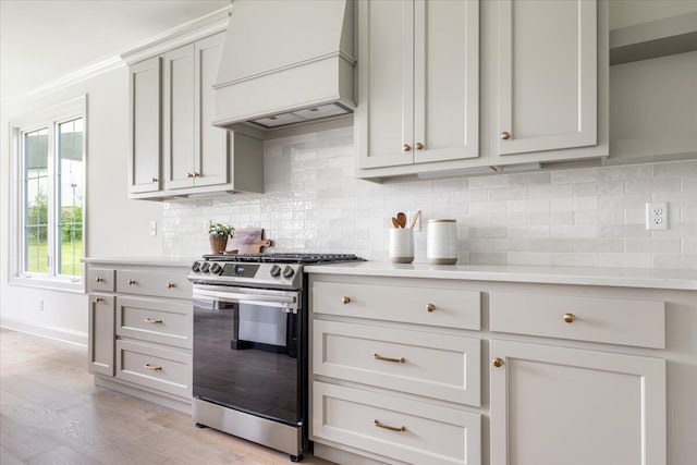 kitchen with custom exhaust hood, a wealth of natural light, stainless steel range with gas stovetop, and light hardwood / wood-style floors