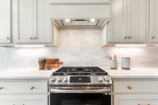 kitchen featuring white cabinetry, stainless steel gas range oven, backsplash, and light stone countertops