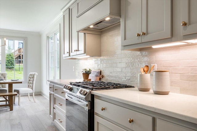 kitchen featuring gas range, premium range hood, light hardwood / wood-style floors, ornamental molding, and light stone counters