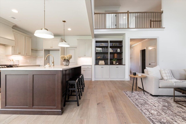 kitchen with ornamental molding, a breakfast bar, a center island with sink, and light hardwood / wood-style floors