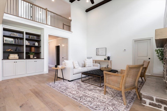 living room with light hardwood / wood-style flooring, a high ceiling, ceiling fan, and beam ceiling