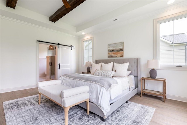 bedroom featuring a barn door, beam ceiling, and light hardwood / wood-style floors