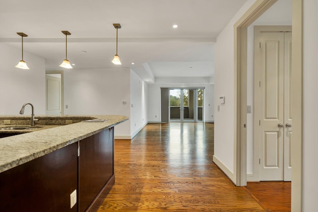 kitchen with dark wood-type flooring, light stone countertops, sink, and decorative light fixtures