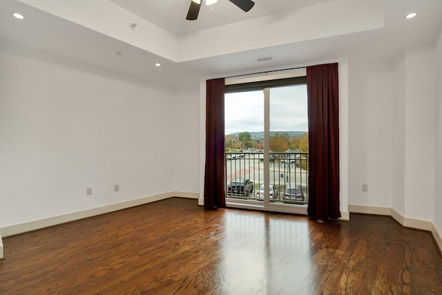 spare room featuring dark hardwood / wood-style flooring, ceiling fan, and a raised ceiling