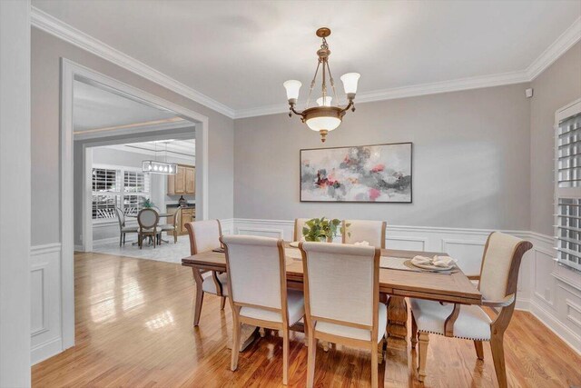 dining area featuring light hardwood / wood-style flooring, crown molding, and a notable chandelier