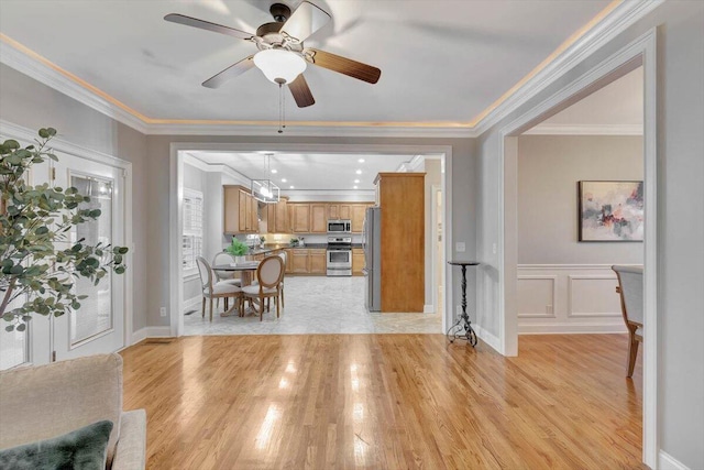 kitchen with light wood-type flooring, stainless steel appliances, ceiling fan, and ornamental molding