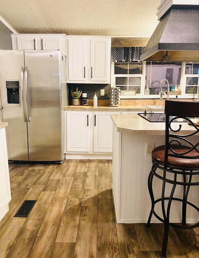 kitchen featuring a kitchen bar, stainless steel fridge, light wood-type flooring, white cabinetry, and range hood