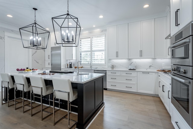 kitchen featuring a center island with sink, white cabinets, light hardwood / wood-style floors, a breakfast bar area, and stainless steel appliances