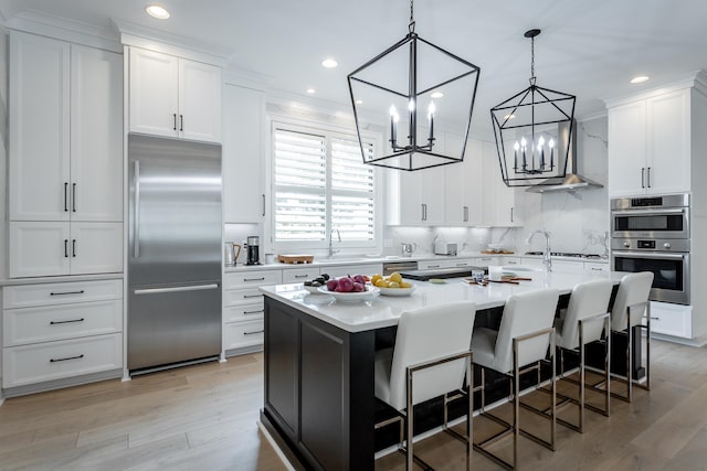 kitchen with a breakfast bar, white cabinets, light hardwood / wood-style flooring, an island with sink, and appliances with stainless steel finishes