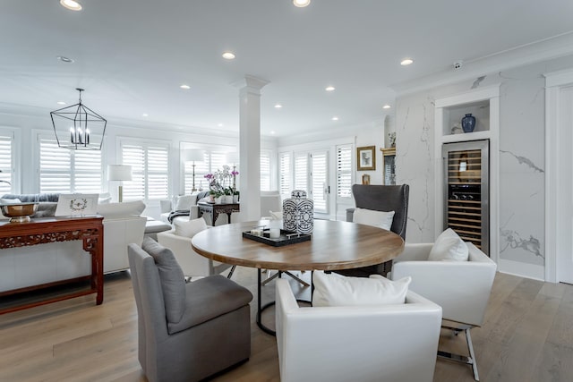 dining room featuring decorative columns, light hardwood / wood-style flooring, ornamental molding, beverage cooler, and a chandelier