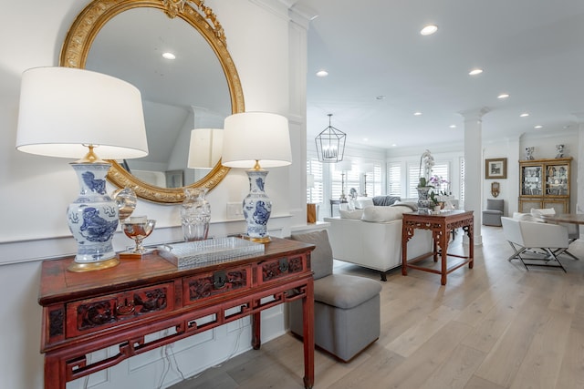 living room featuring light wood-type flooring, decorative columns, ornamental molding, and a notable chandelier