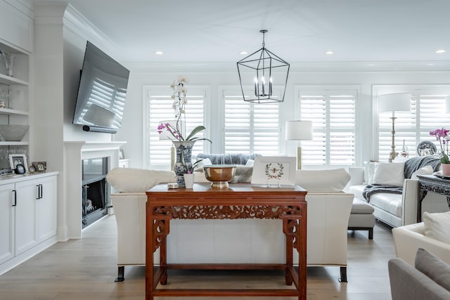 living room featuring built in shelves, ornamental molding, light hardwood / wood-style floors, and a notable chandelier