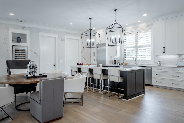 kitchen with pendant lighting, dishwasher, white cabinetry, and an island with sink