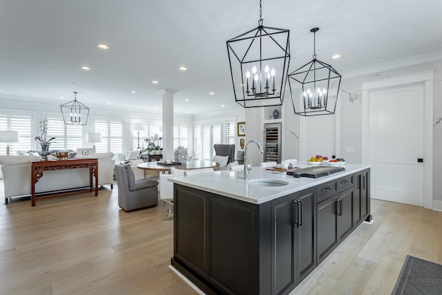 kitchen featuring light wood-type flooring, decorative columns, sink, a center island with sink, and hanging light fixtures