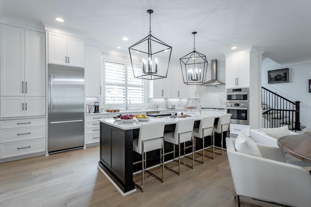 kitchen featuring appliances with stainless steel finishes, a kitchen island, wall chimney range hood, white cabinetry, and a breakfast bar area