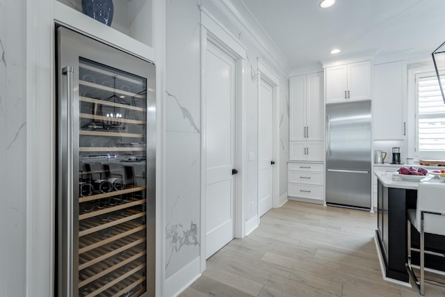 interior space with white cabinetry, beverage cooler, stainless steel built in refrigerator, light hardwood / wood-style floors, and ornamental molding