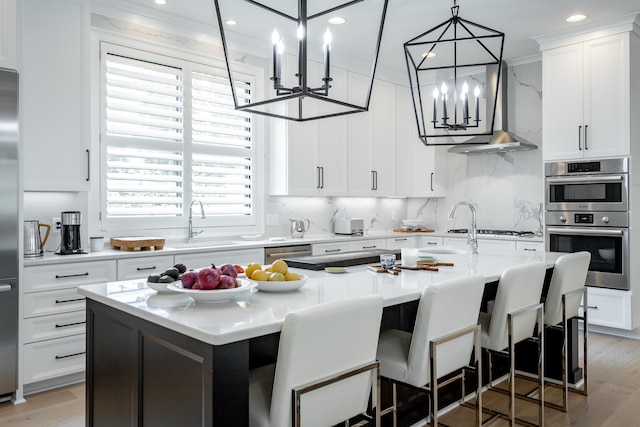 kitchen featuring a kitchen island with sink, an inviting chandelier, white cabinets, a kitchen breakfast bar, and decorative light fixtures