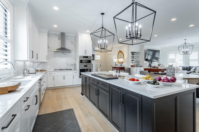 kitchen with a kitchen island with sink, sink, wall chimney range hood, light hardwood / wood-style floors, and white cabinetry