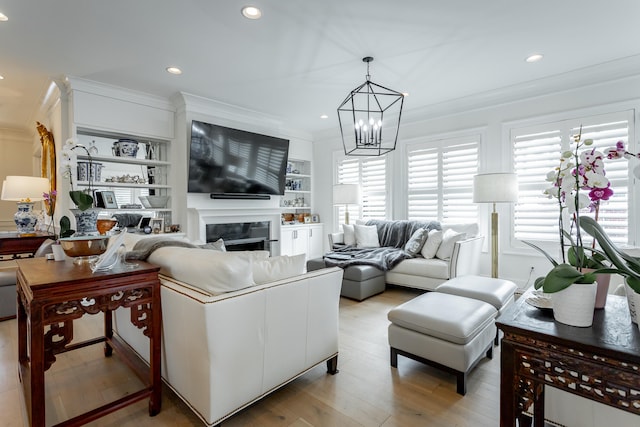 living room featuring built in shelves, crown molding, light hardwood / wood-style floors, and an inviting chandelier