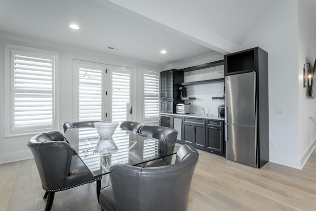 dining room featuring bar, light hardwood / wood-style floors, and vaulted ceiling