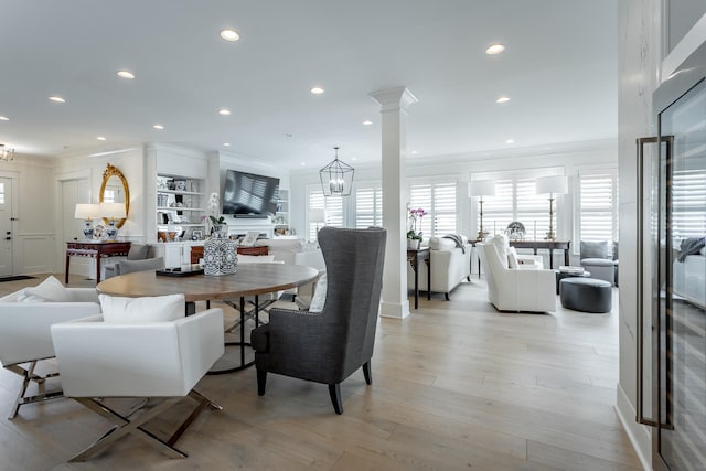 dining area with decorative columns, light hardwood / wood-style flooring, ornamental molding, and a notable chandelier