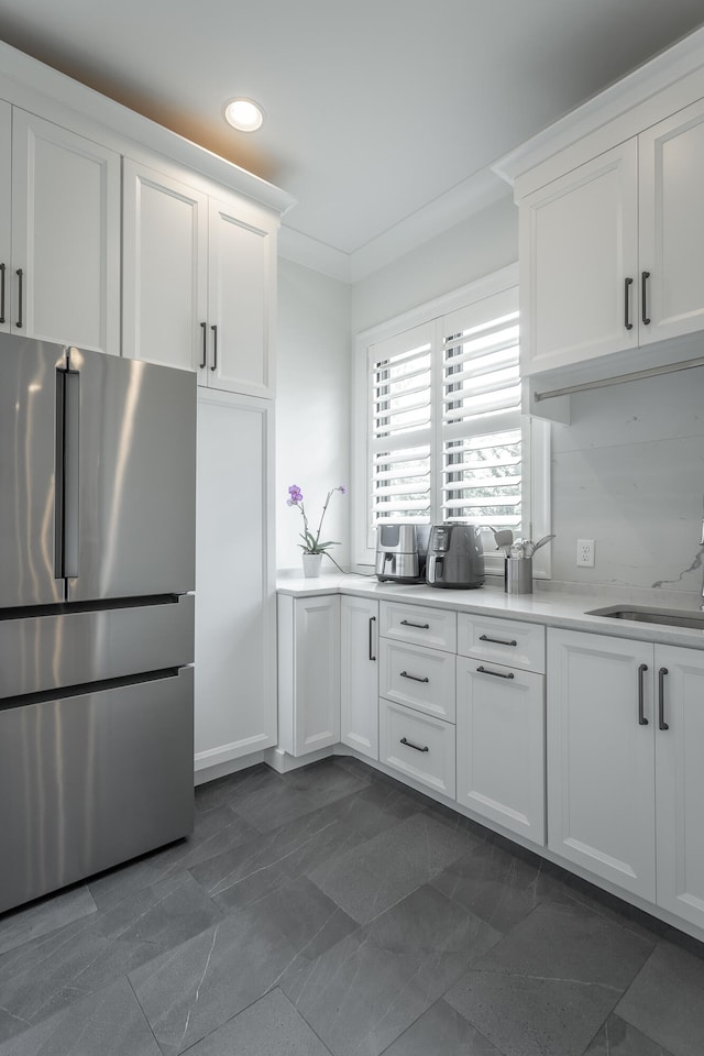 kitchen featuring stainless steel fridge, white cabinetry, ornamental molding, and sink