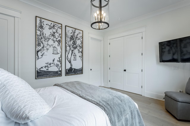 bedroom with a closet, crown molding, light hardwood / wood-style flooring, and an inviting chandelier