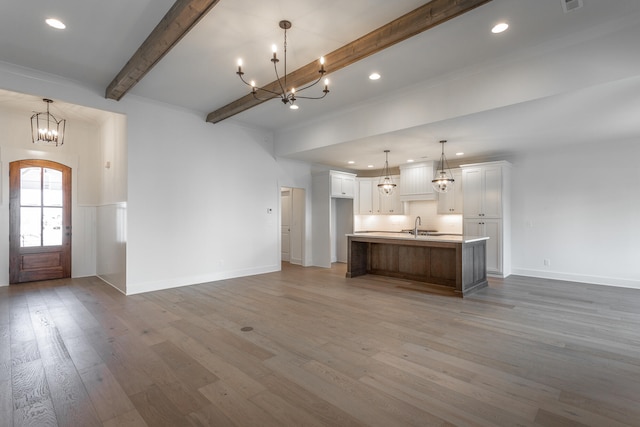 kitchen with white cabinets, beam ceiling, wood-type flooring, a large island with sink, and decorative light fixtures