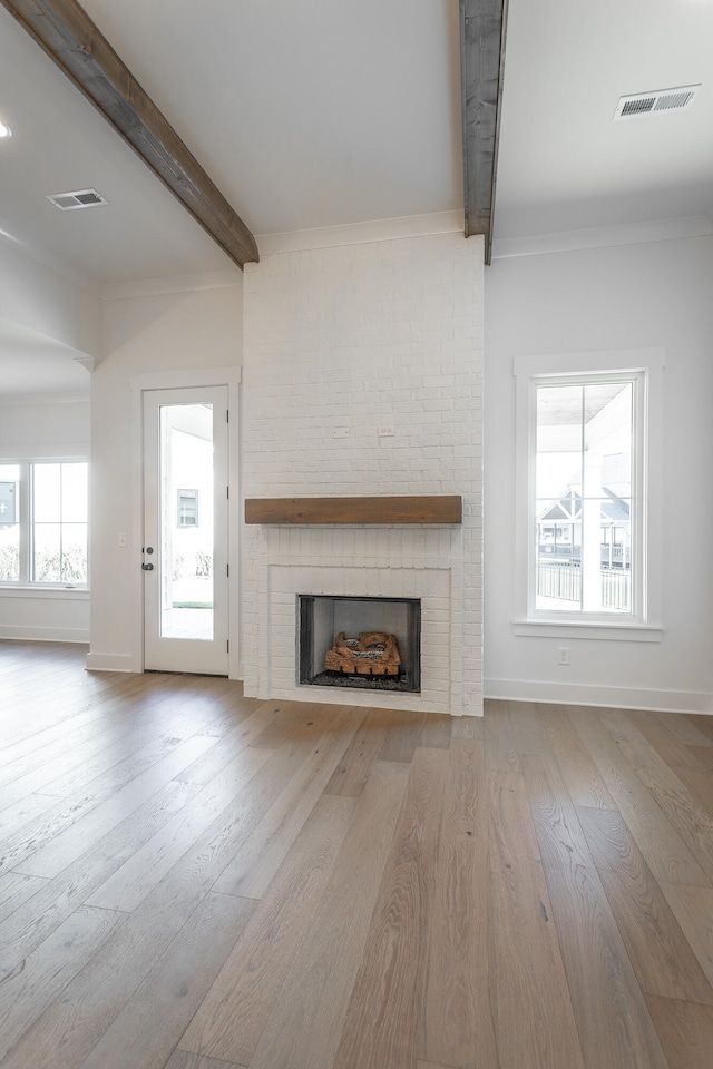 unfurnished living room with light hardwood / wood-style floors, beamed ceiling, a brick fireplace, and plenty of natural light