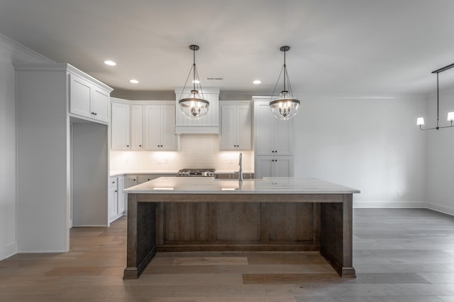 kitchen featuring light hardwood / wood-style flooring, a center island with sink, decorative light fixtures, white cabinetry, and stainless steel range oven