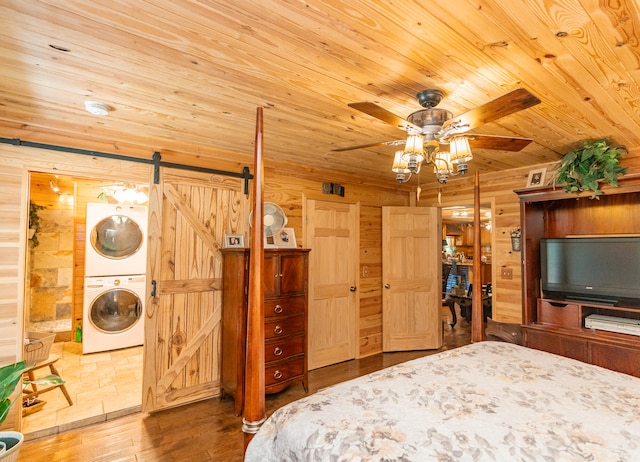 unfurnished bedroom featuring ensuite bathroom, a barn door, hardwood / wood-style floors, stacked washer / dryer, and wood walls