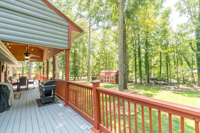 deck featuring a grill, ceiling fan, a lawn, and a shed