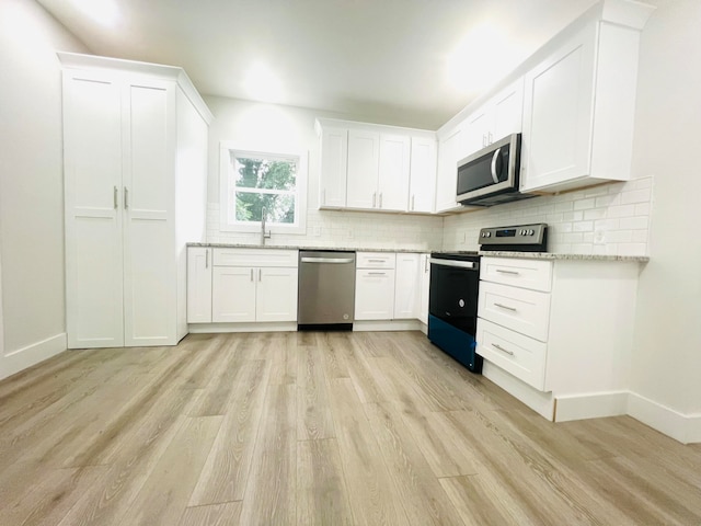 kitchen with white cabinetry, light hardwood / wood-style flooring, light stone counters, and stainless steel appliances