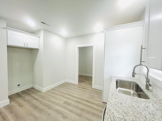 kitchen with light stone counters, light hardwood / wood-style floors, white cabinetry, and sink