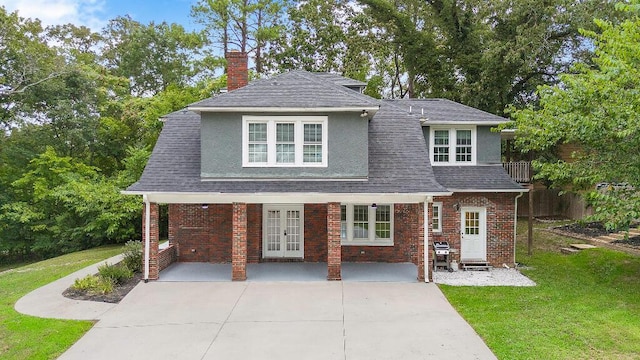 view of front of house with stucco siding, a front lawn, french doors, roof with shingles, and brick siding