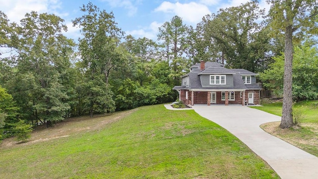 view of front facade featuring brick siding, concrete driveway, a chimney, and a front yard